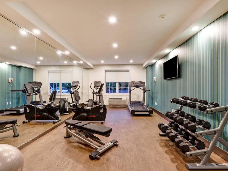 Ein Fitnessstudio mit Cardiogeräten, Kurzhanteln und einer Spiegelwand.