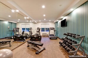 A gym with cardio machines, dumbbells, and a mirrored wall.