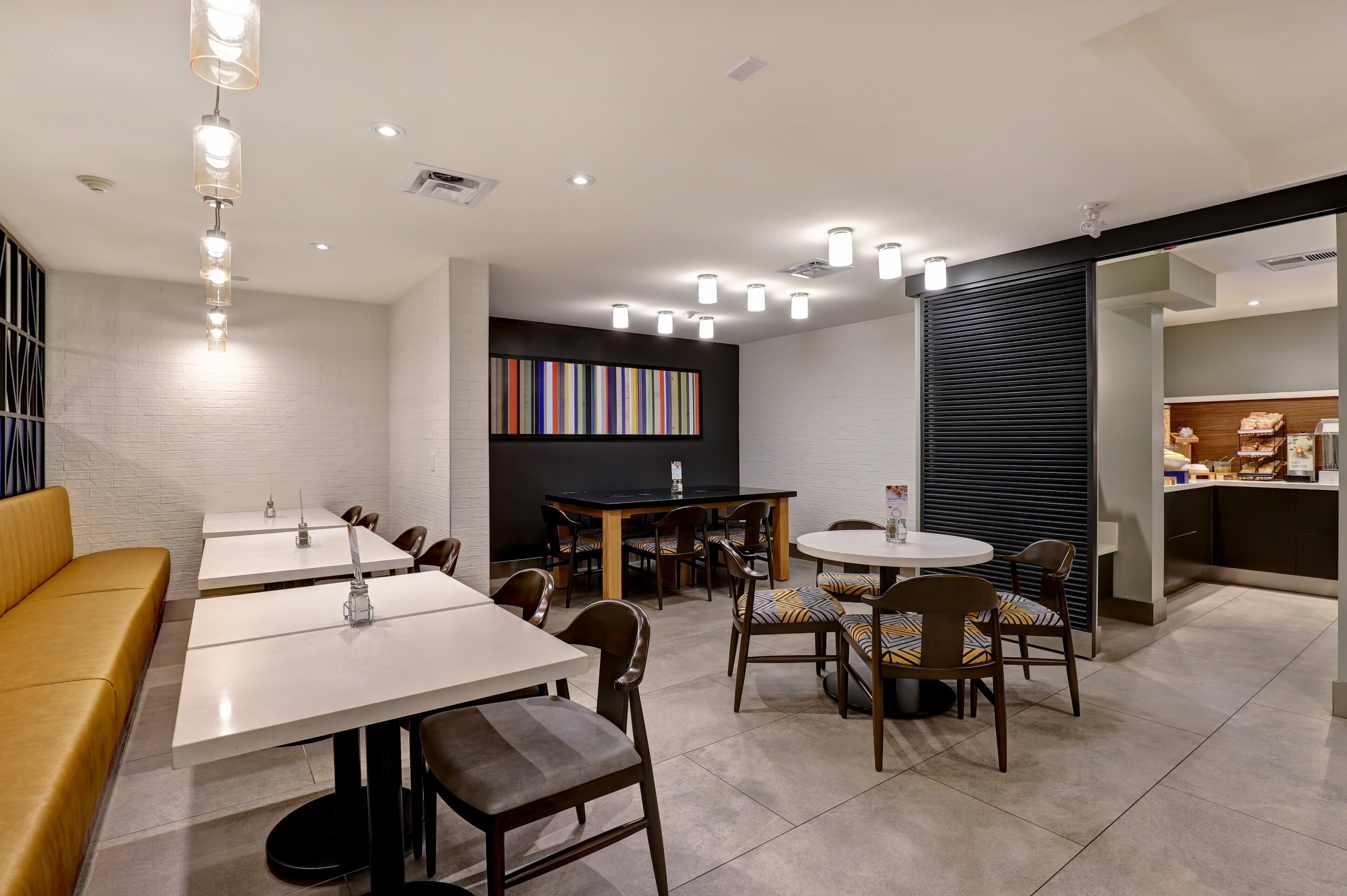 A modern dining area with multiple tables and chairs, a sofa, and a bookshelf with colorful books.
