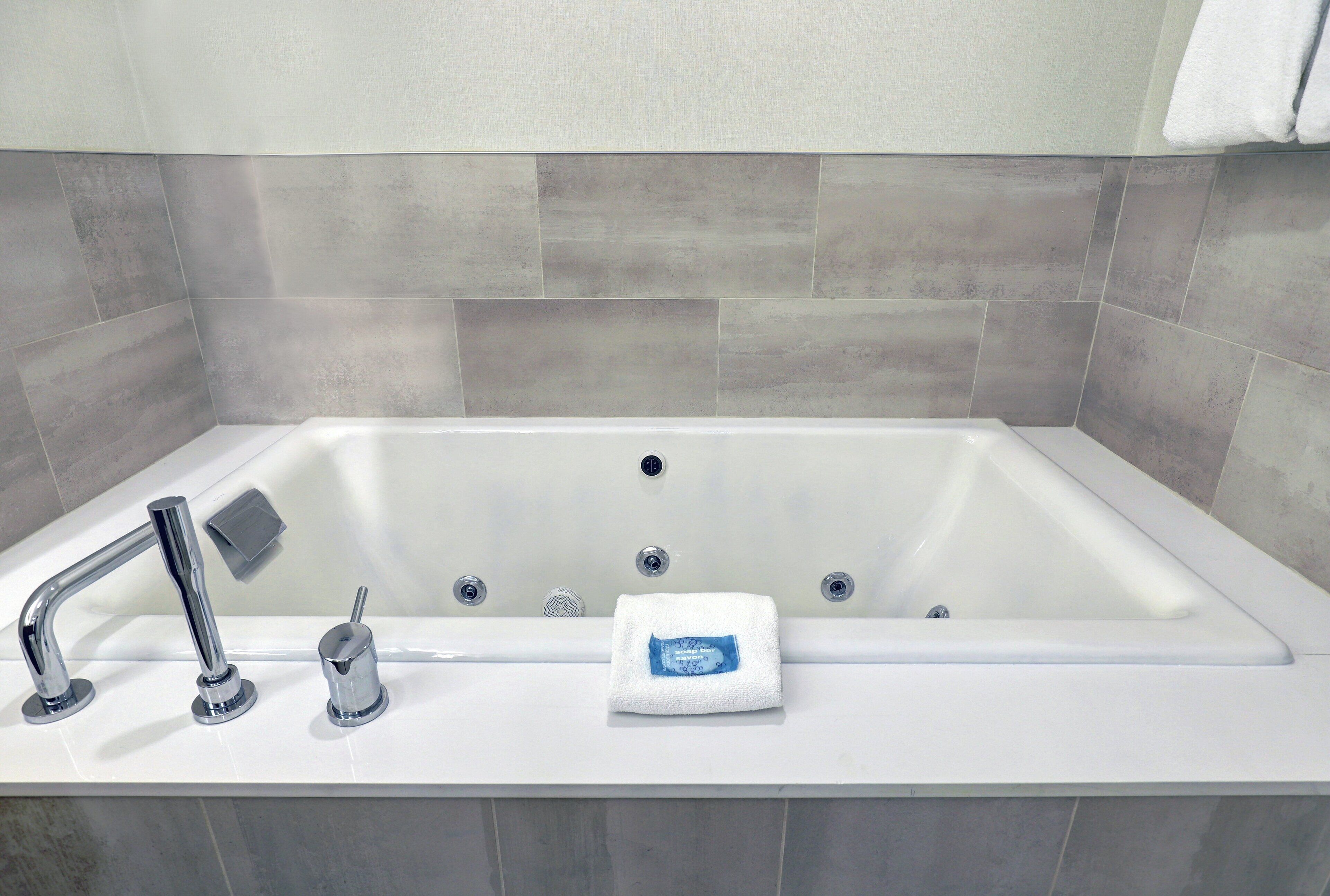Un baño moderno con una bañera grande, un cabezal de ducha manual y una toalla con etiqueta azul.
