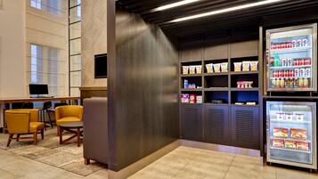 A hotel lobby with seating, a refrigerator stocked with beverages, and a wall-mounted television.
