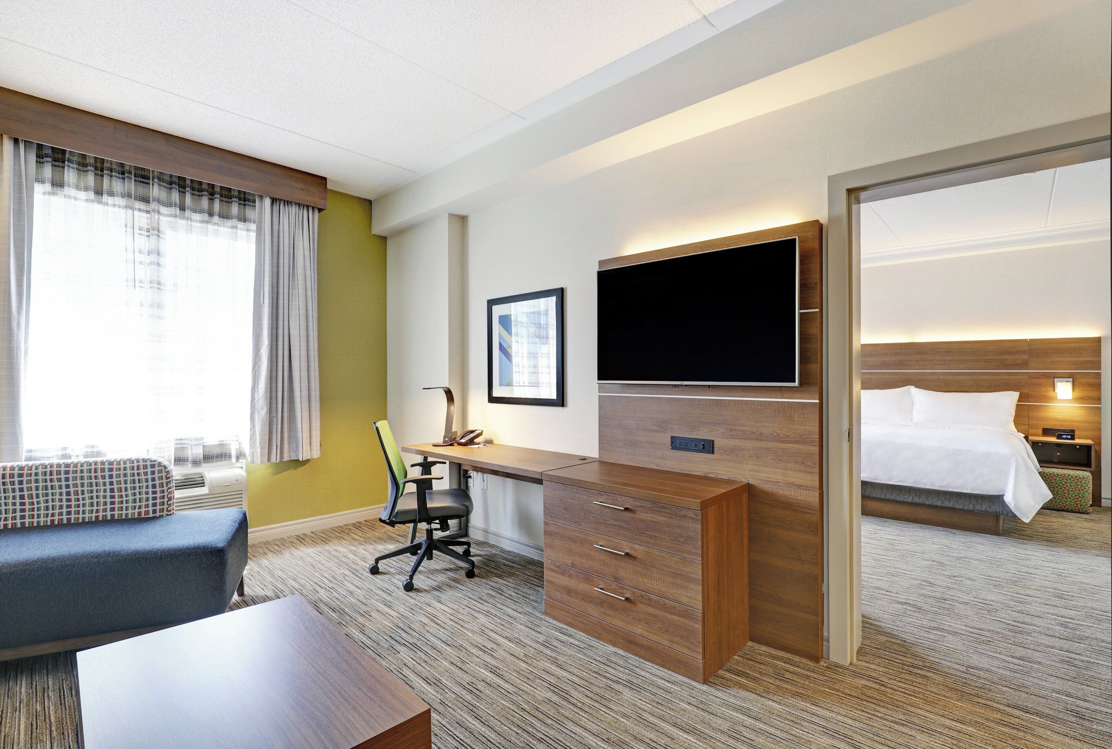 Une chambre d’hôtel comprenant un lit, un bureau avec une chaise, une télévision et une fenêtre avec des rideaux.