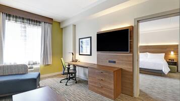 A hotel room with a bed, a desk with a chair, a television, and a window with curtains.