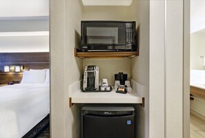 A hotel room with a bed, a minibar, a microwave, a coffee maker, and a refrigerator.