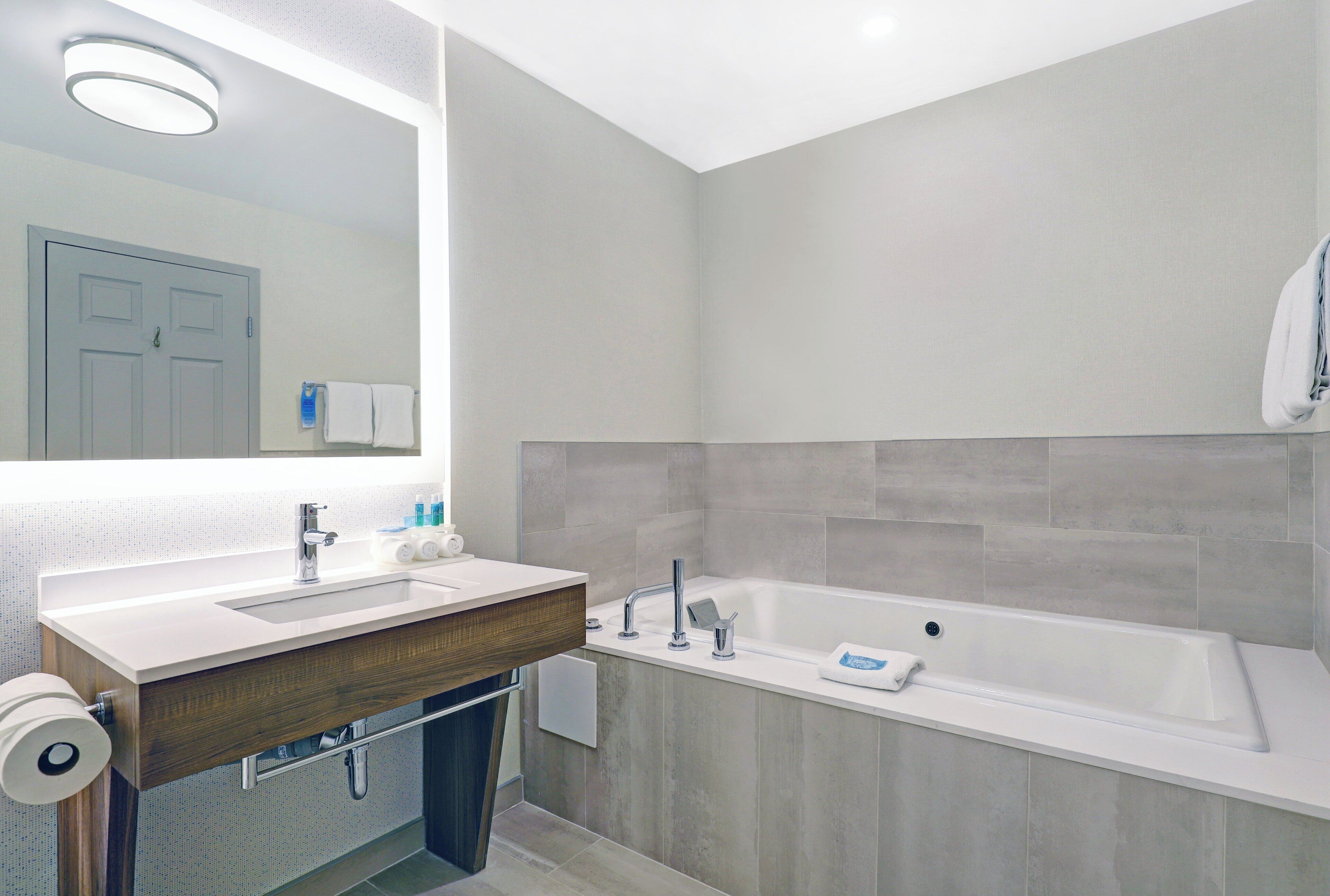 A modern bathroom with a large mirror, a sink, a bathtub, and a toilet.