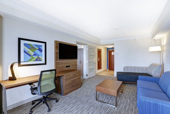 A hotel room with a wooden desk, a black office chair, a television, a blue sofa, and a small table.