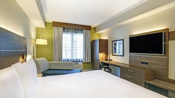 Ein Hotelzimmer mit einem großen Bett, einem Schreibtisch, einem Fernseher und einem Fenster mit Vorhängen.