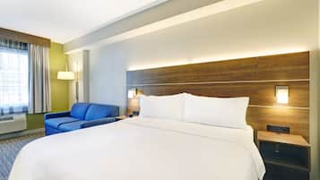 Una habitación de hotel con una cama grande, un sillón azul, una mesita de noche con lámpara y un cabecero de madera.