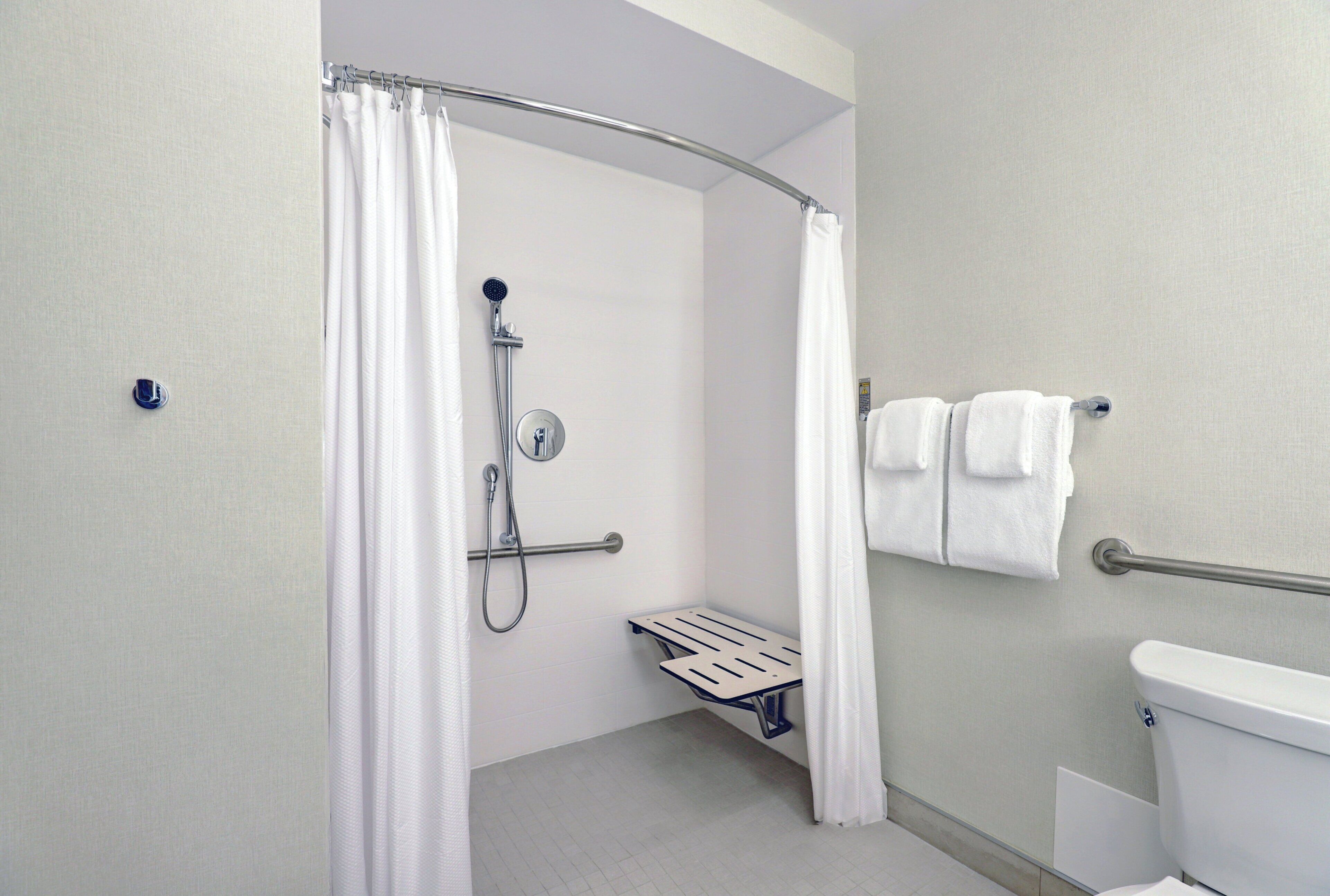 Een badkamer met douche, toilet en een klein bankje.