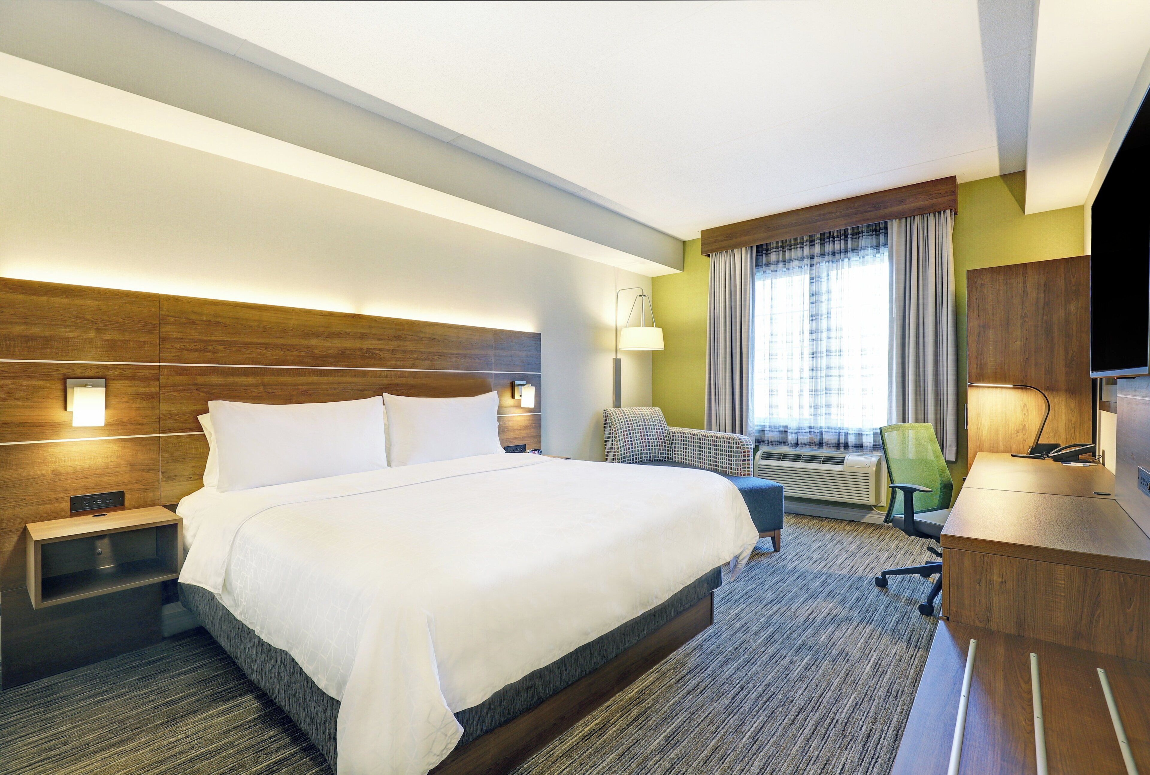A hotel room with a large bed, a desk, a chair, a flat-screen TV, and a window with curtains.