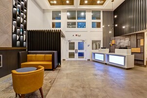 A hotel lobby with a reception desk, a seating area with a sofa and armchair, and a large window with multiple panes.