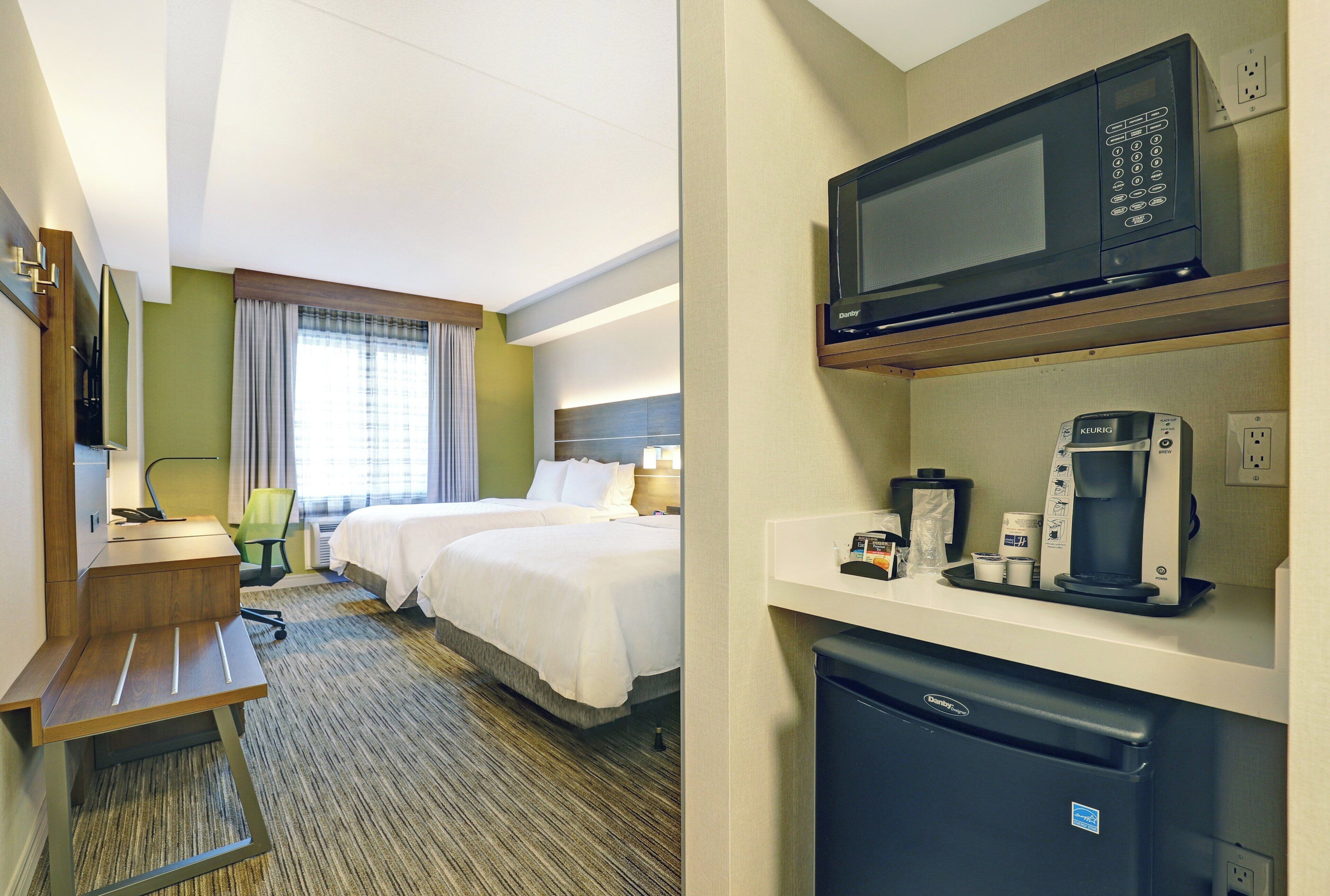 Una habitación de hotel con una cama, un escritorio, un microondas, una cafetera y un refrigerador.