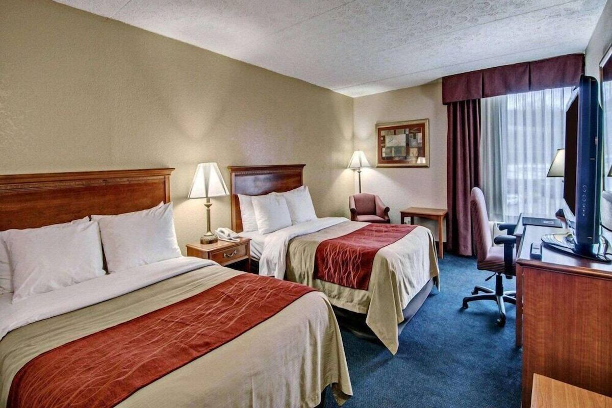 Habitación de hotel con dos camas, un escritorio con computadora, una silla y televisor.