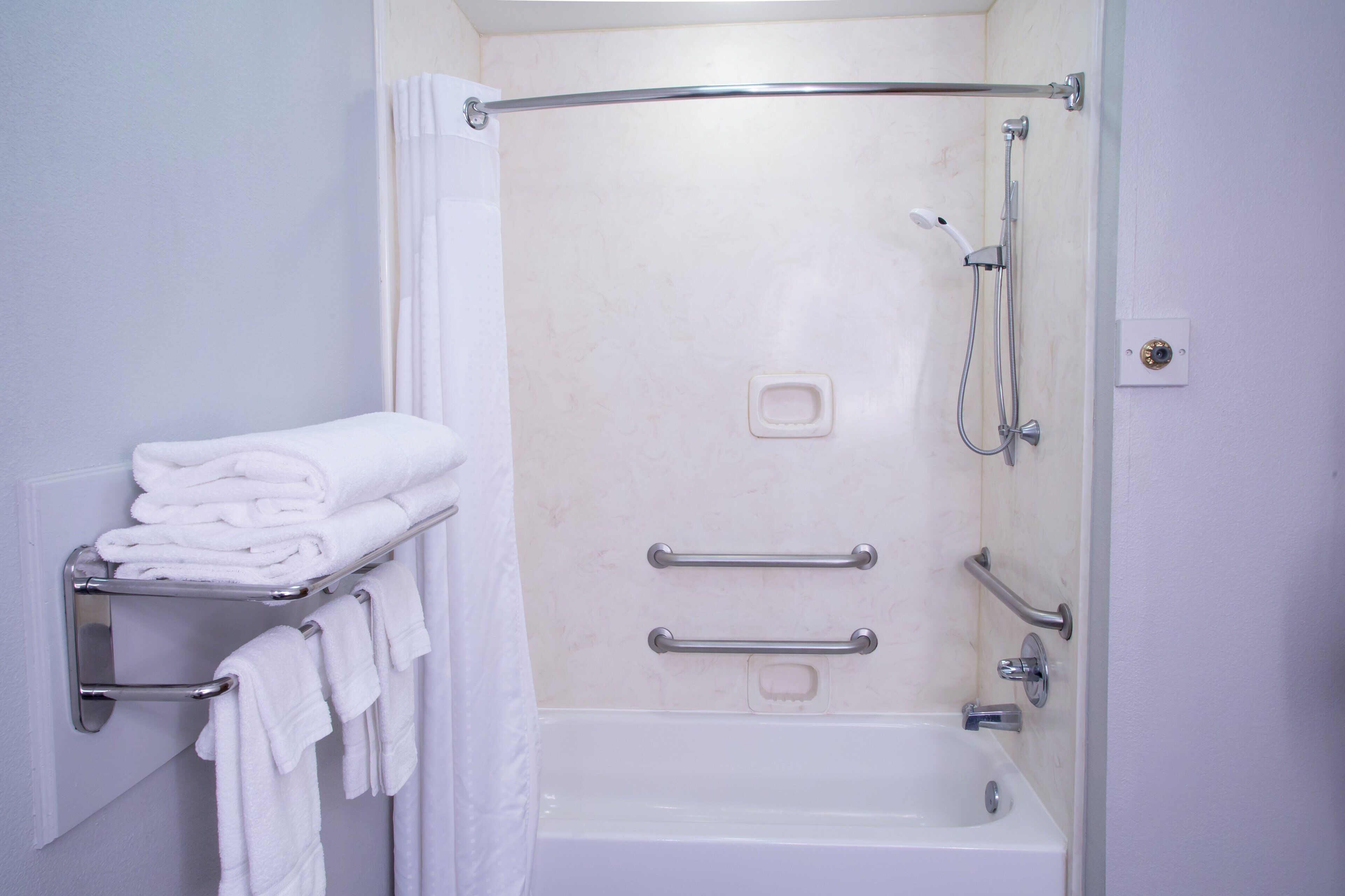A bathroom with a bathtub, a shower, and a towel rack with folded towels.