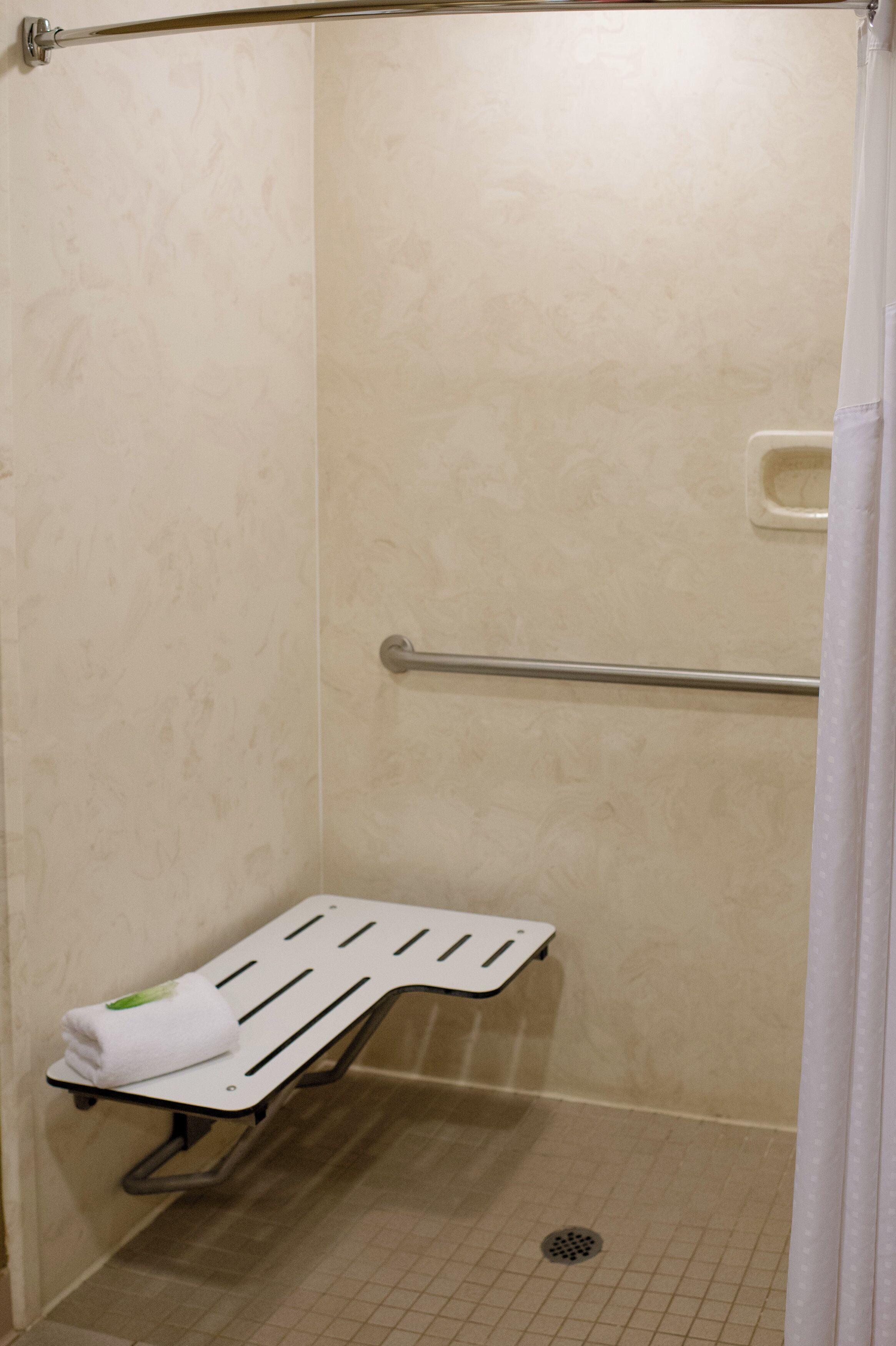 Una cabina de ducha con barra de apoyo, una toalla blanca y un desagüe en el suelo.