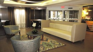 Un hall d’entrée avec un canapé, deux fauteuils, une petite table sur laquelle est posé un vase, et un tapis à motifs.