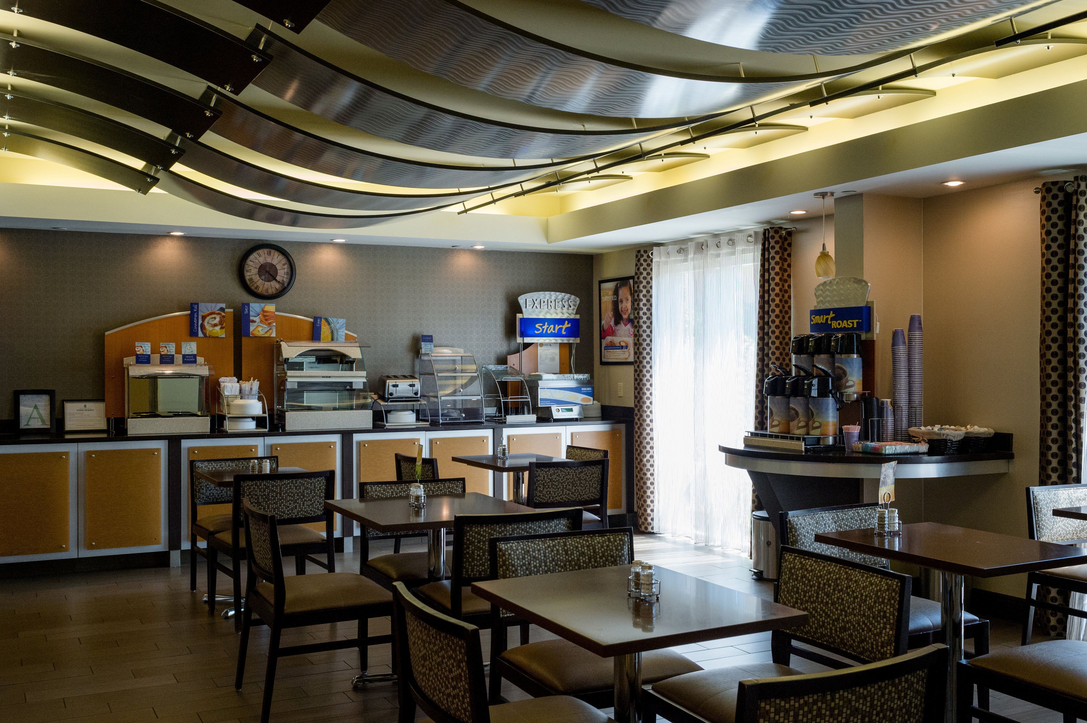 A hotel lobby with a reception desk, self-service coffee machines, and seating areas.