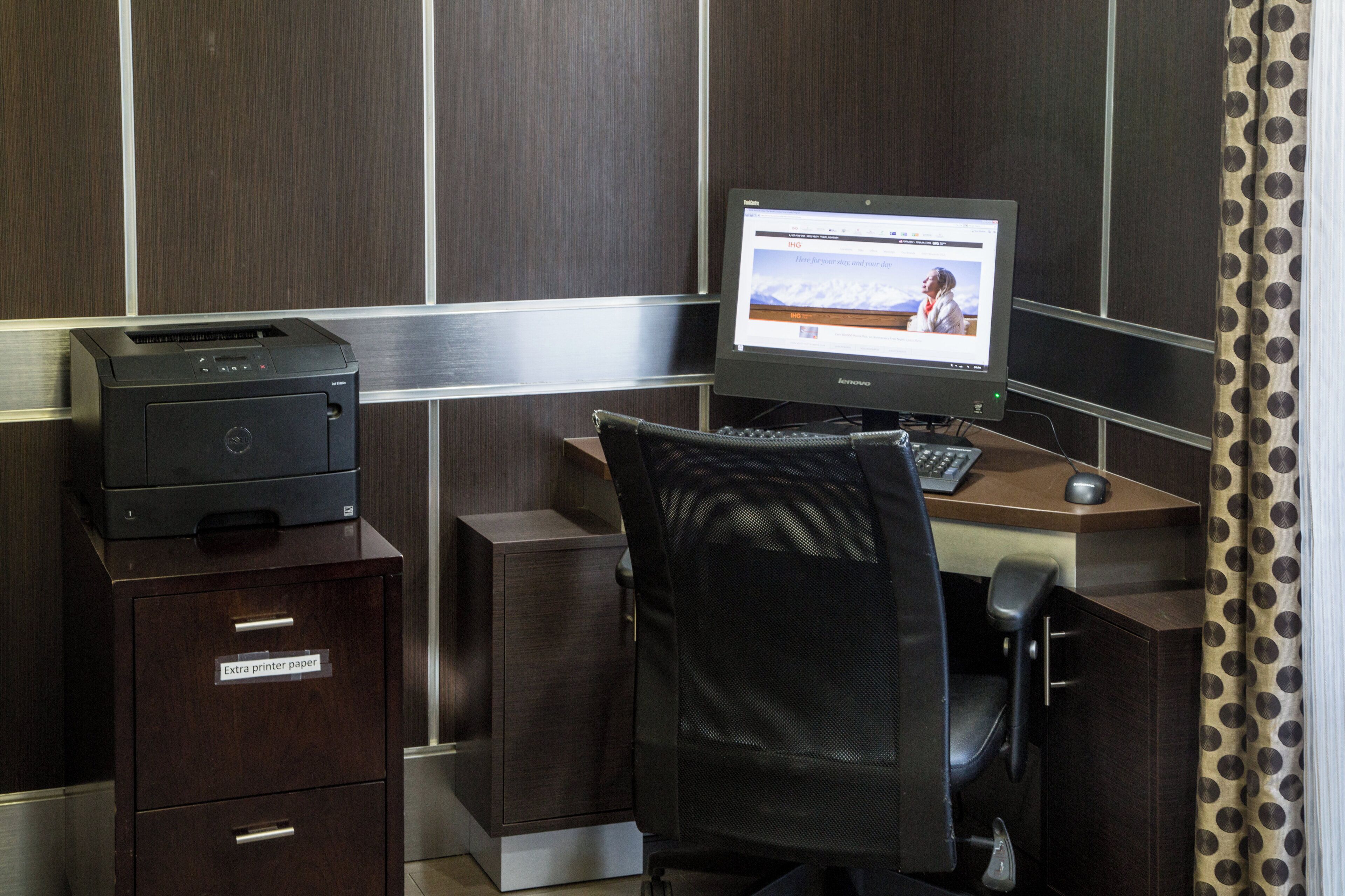 Een hotelkamer met een bureau, computer, printer en een stoel.