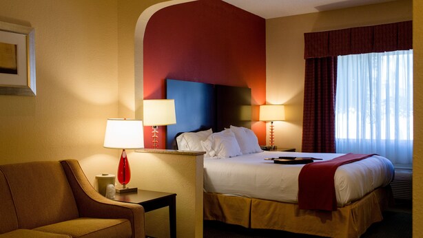A hotel room with a bed, a sofa, two bedside tables with lamps, and a window with curtains. - Holiday Inn Express Hotel & Suites Oxford by IHG (Oxford)