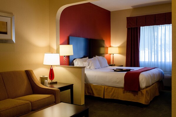 A hotel room with a bed, a sofa, two bedside tables with lamps, and a window with curtains.