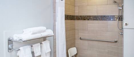 Un espace douche avec un rideau de douche blanc, une chaise blanche et un porte-serviettes avec des serviettes pliées.