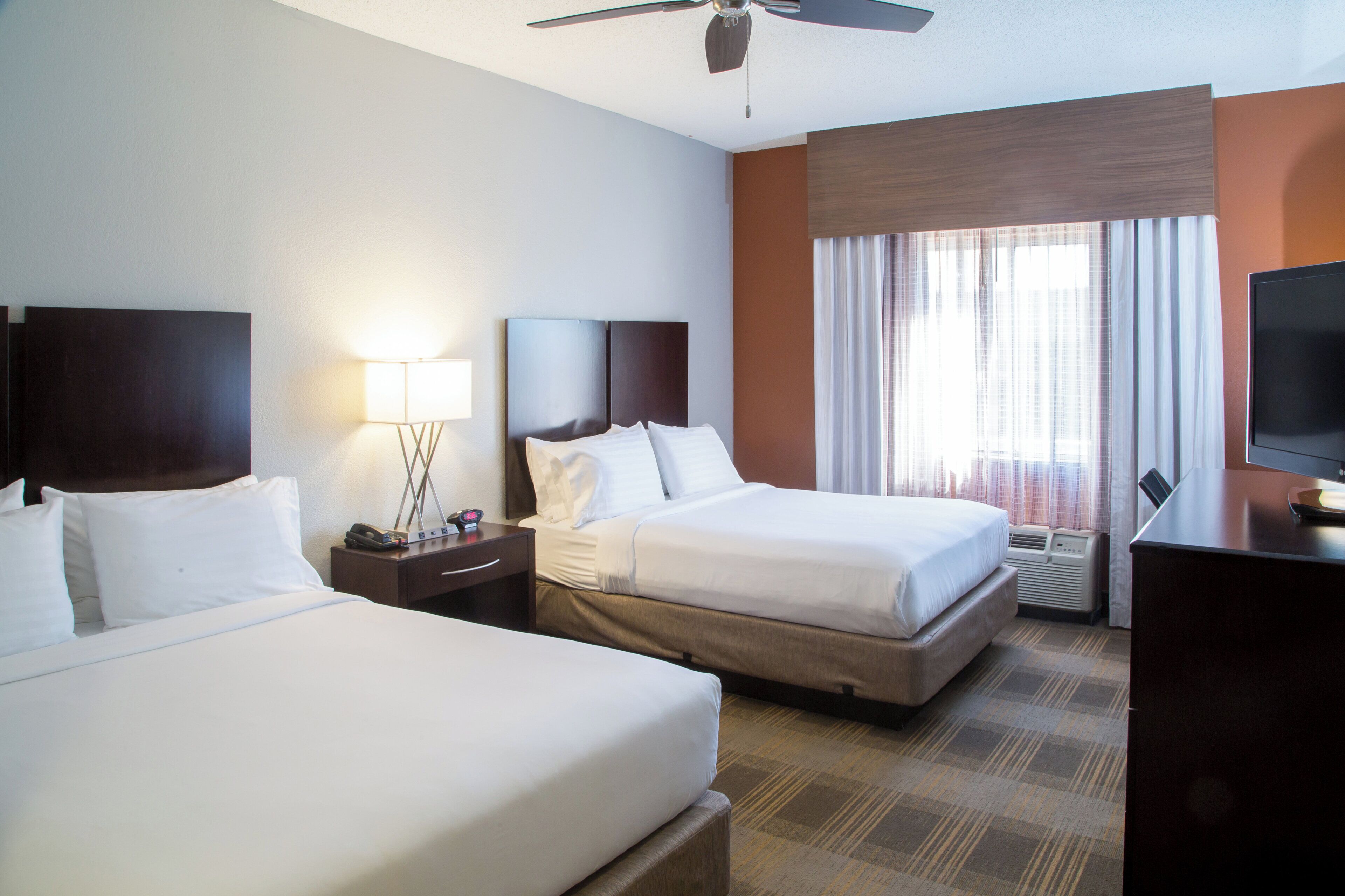 A hotel room with two beds, a desk, a television, and a window with curtains.