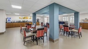 A spacious dining area with multiple tables and chairs, a kitchen area in the background, and a large pillar in the center. - Comfort Inn US Hwy 80 (Demopolis)