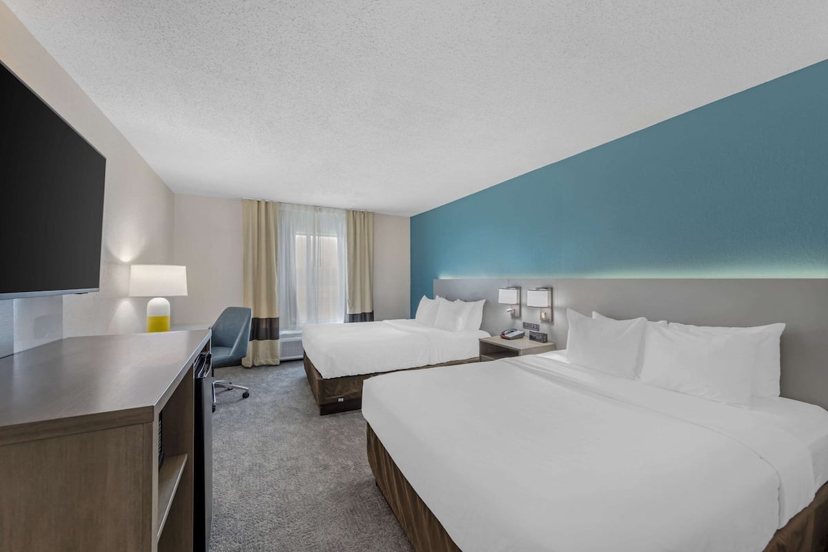 A hotel room with two beds, a desk, a chair, a TV, and a window with curtains.
