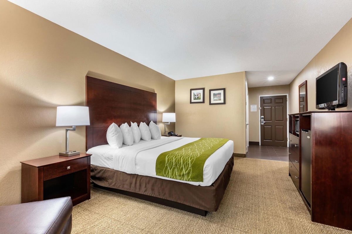 A hotel room with a bed, bedside tables, a desk, a chair, a television, and a door leading to the bathroom.