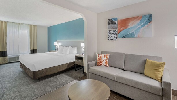 A hotel room with a bed, a sofa, a coffee table, and artwork on the wall. - Comfort Inn US Hwy 80 (Demopolis)