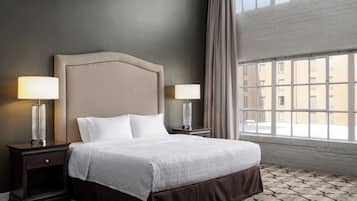 A hotel room with a large bed, two bedside lamps, a window with a view of buildings, and a patterned carpet.