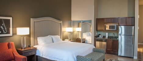 A hotel room with a bed, bedside tables, a desk, a chair, a kitchenette, and a patterned floor.