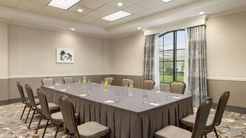 A conference room with a long table, chairs, and a window with curtains.