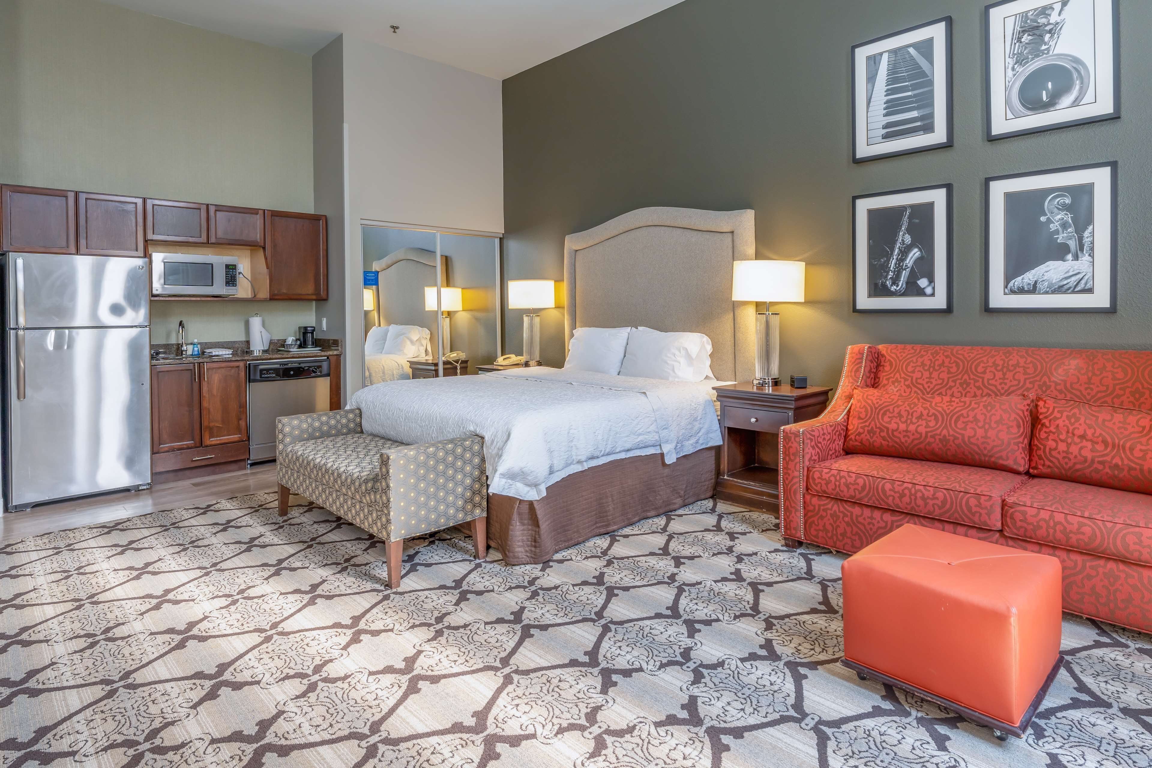 A hotel room with a bed, a sofa, a small table, a nightstand, a mirror, a kitchen area with a refrigerator and microwave, and a patterned floor.
