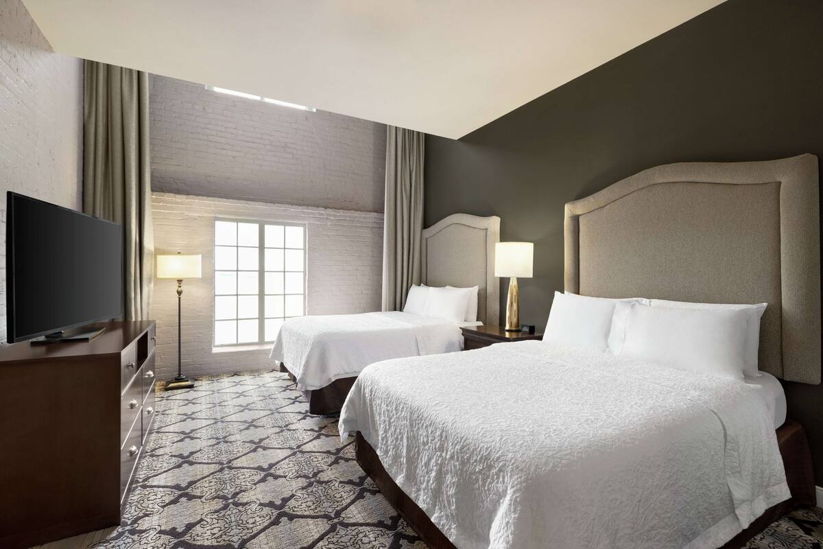 A hotel room with two beds, a TV, a window with curtains, and a patterned carpet.