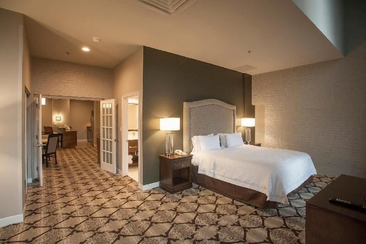 A hotel room with a large bed, a bedside table, a lamp, and a carpeted floor.