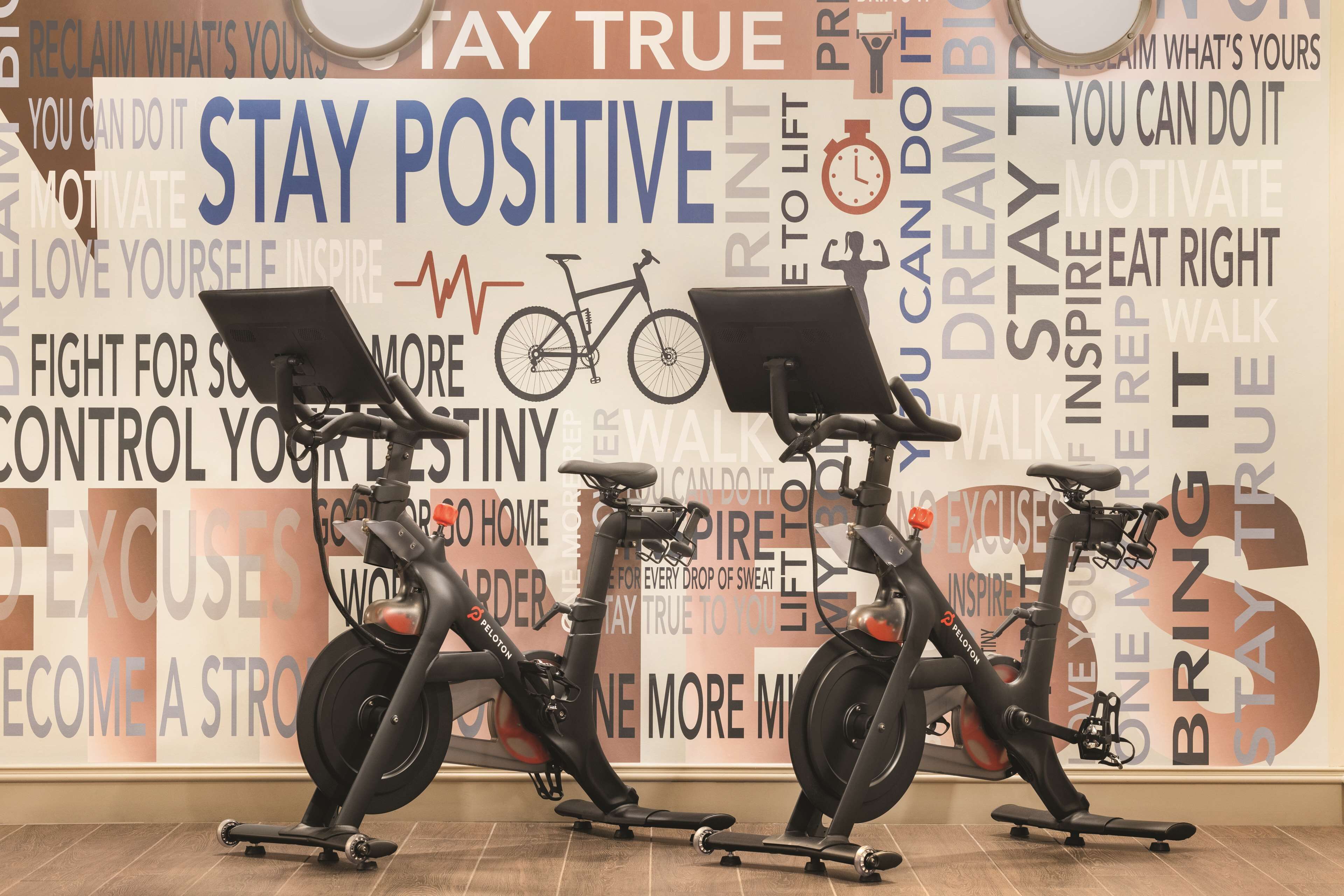 Three stationary bikes in a gym with motivational posters on the wall.