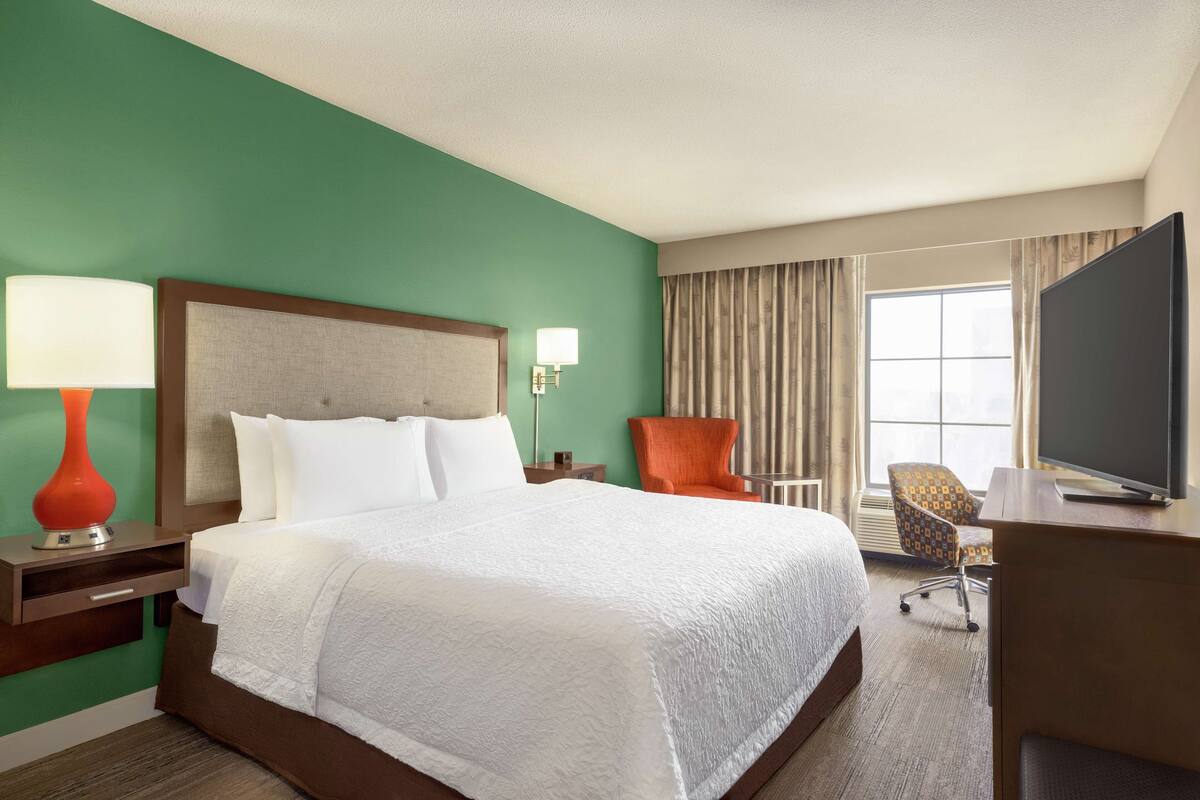 A hotel room with a large bed, a desk, a television, and a chair.