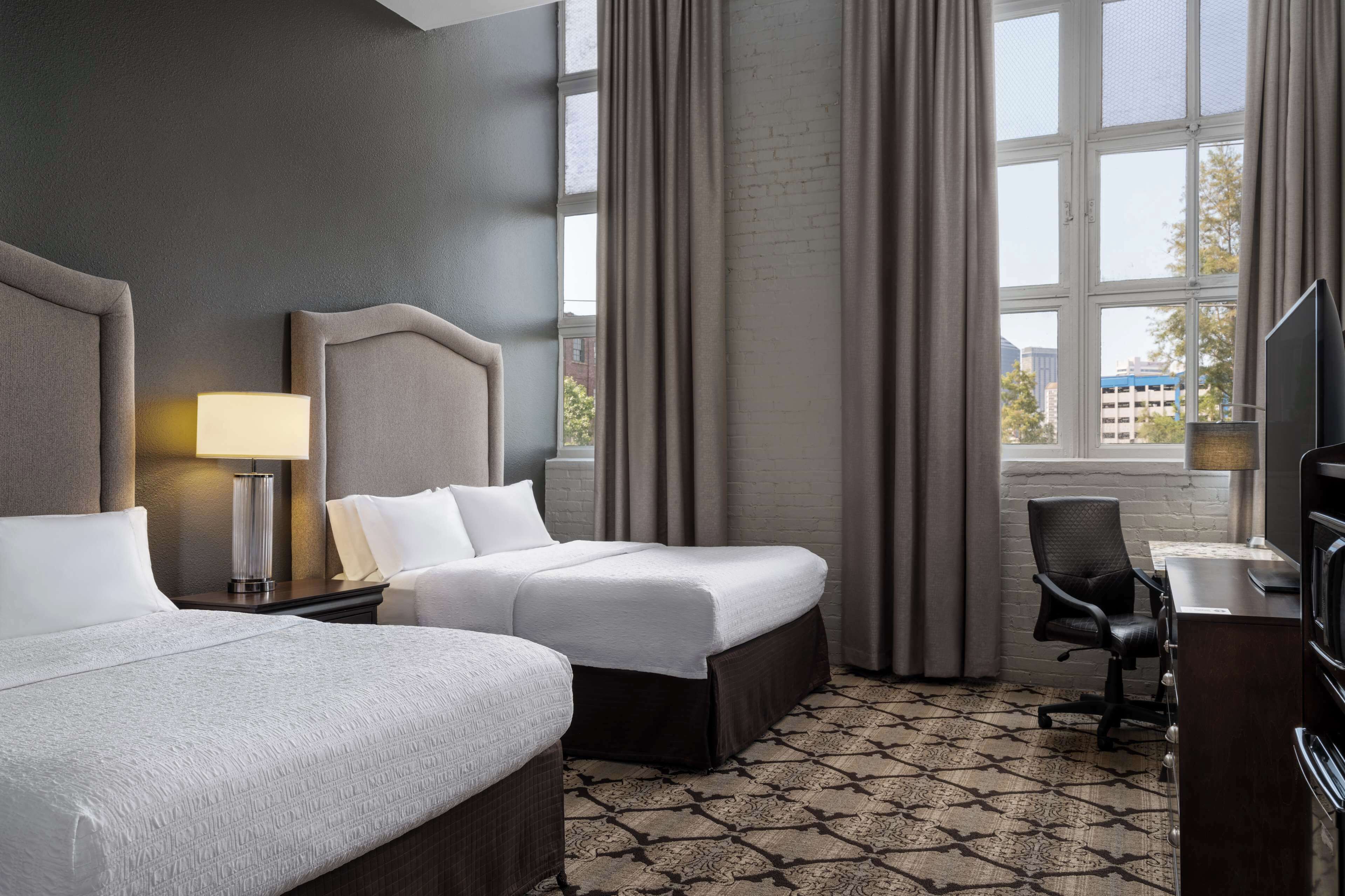 A hotel room with two beds, a desk, a chair, and a television.