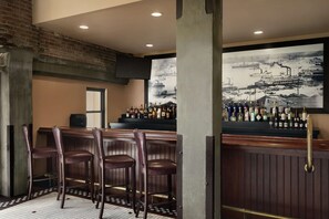 A bar area with wooden bar stools, a tiled floor, and a large black and white maritime painting on the wall.