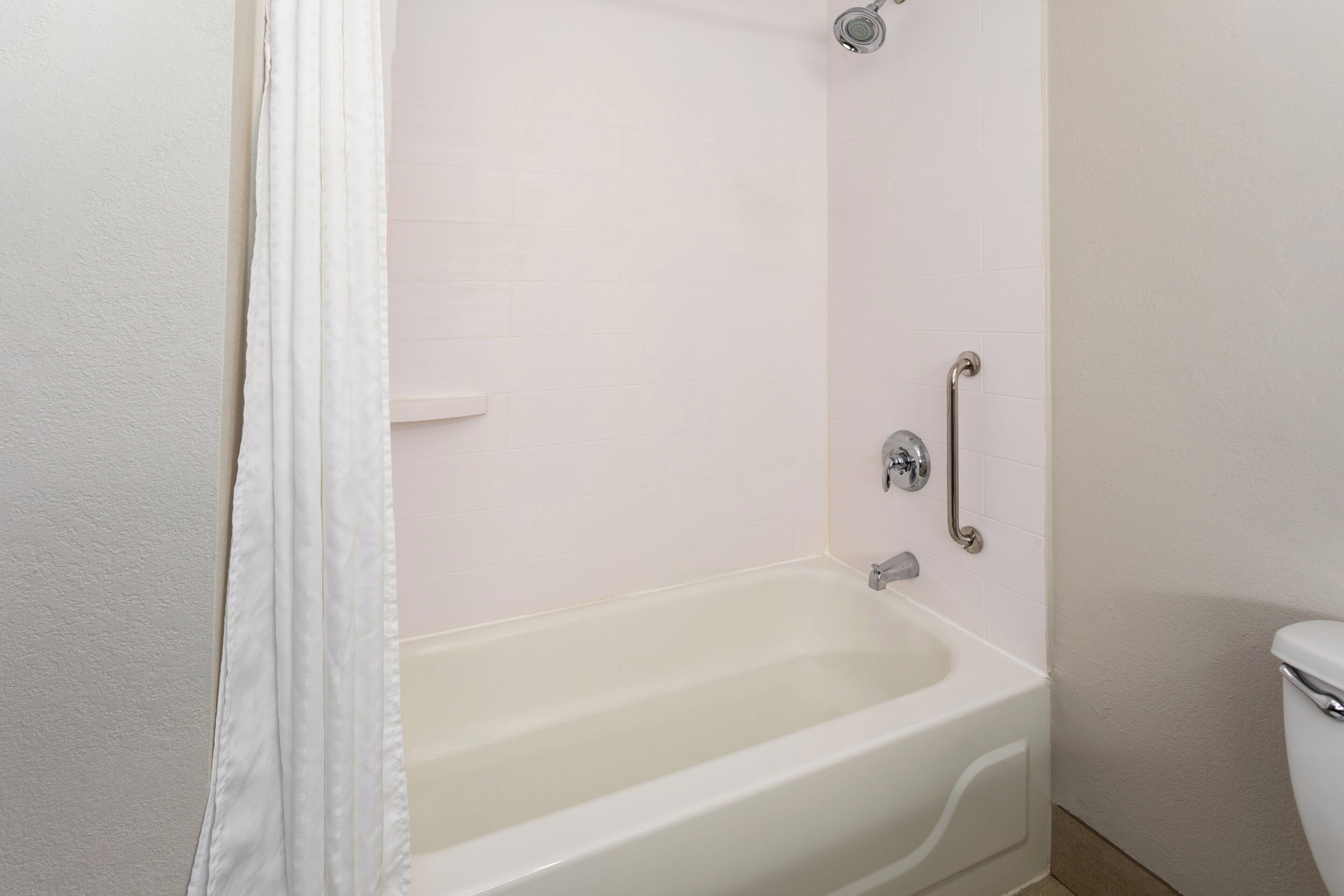 Une baignoire blanche avec un rideau de douche, une barre d’appui et un robinet fixé au mur.