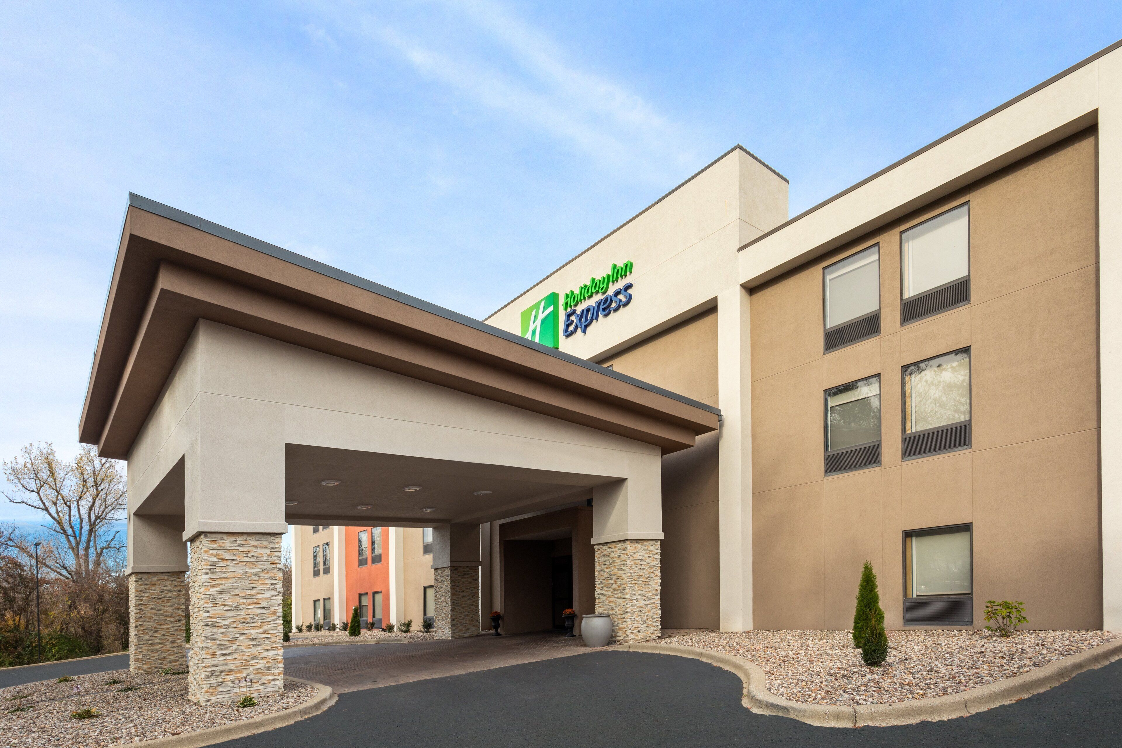 Edificio de Holiday Inn Express con entrada cubierta, pilares de piedra y cielo despejado.