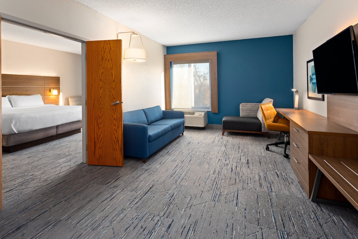 A hotel room with a bed, a blue sofa, a wooden desk, and a television.