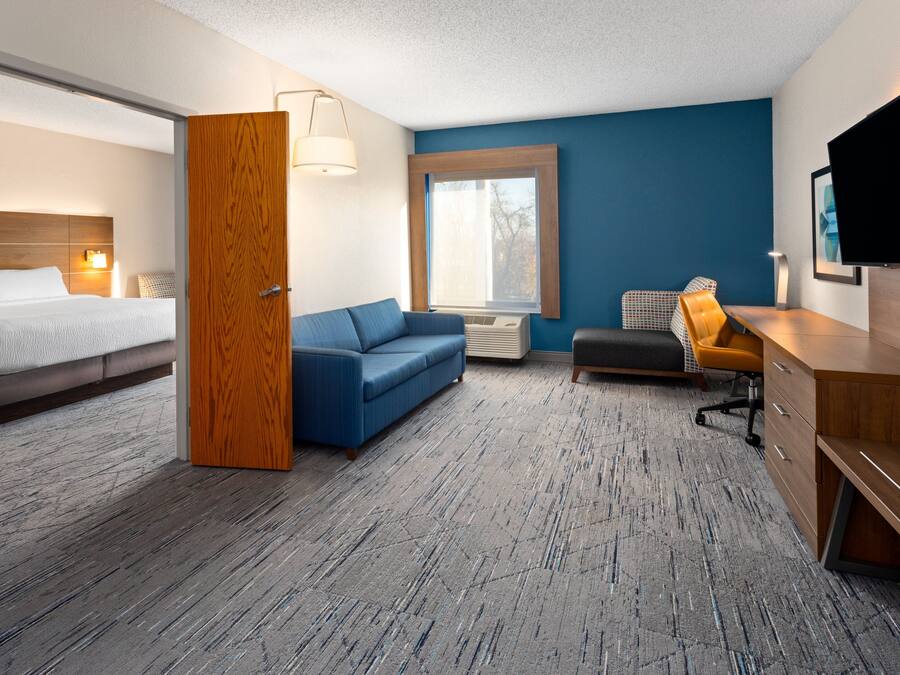 A hotel room with a bed, a blue sofa, a wooden desk, and a television.