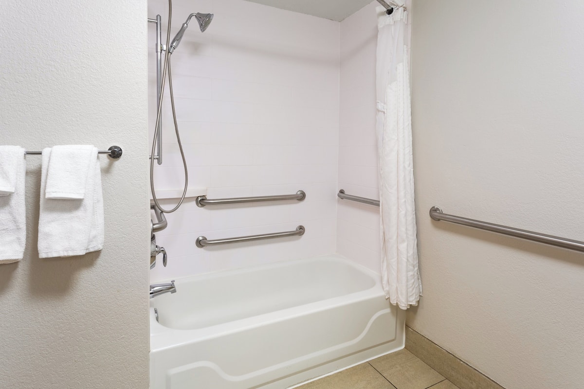 A bathroom with a bathtub, grab bars, a showerhead, and a towel rack.