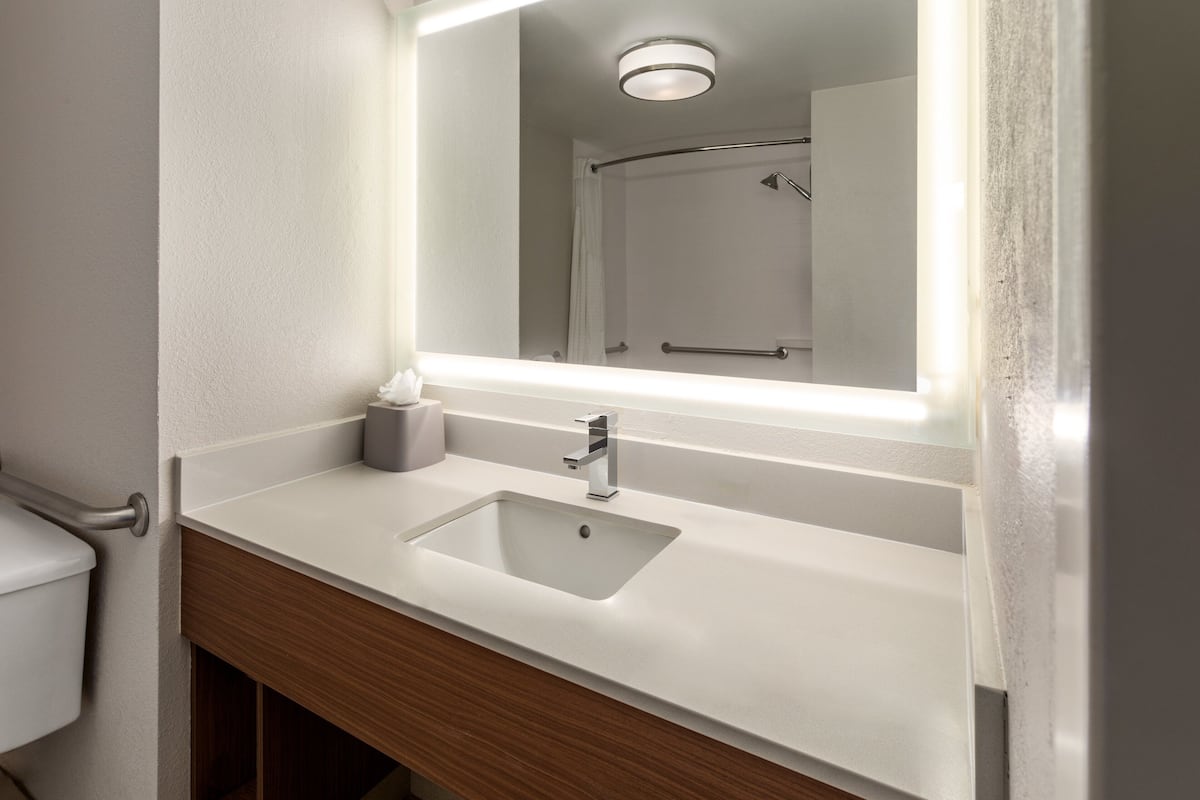 A bathroom with a white sink, a mirror, and a shower visible in the reflection.