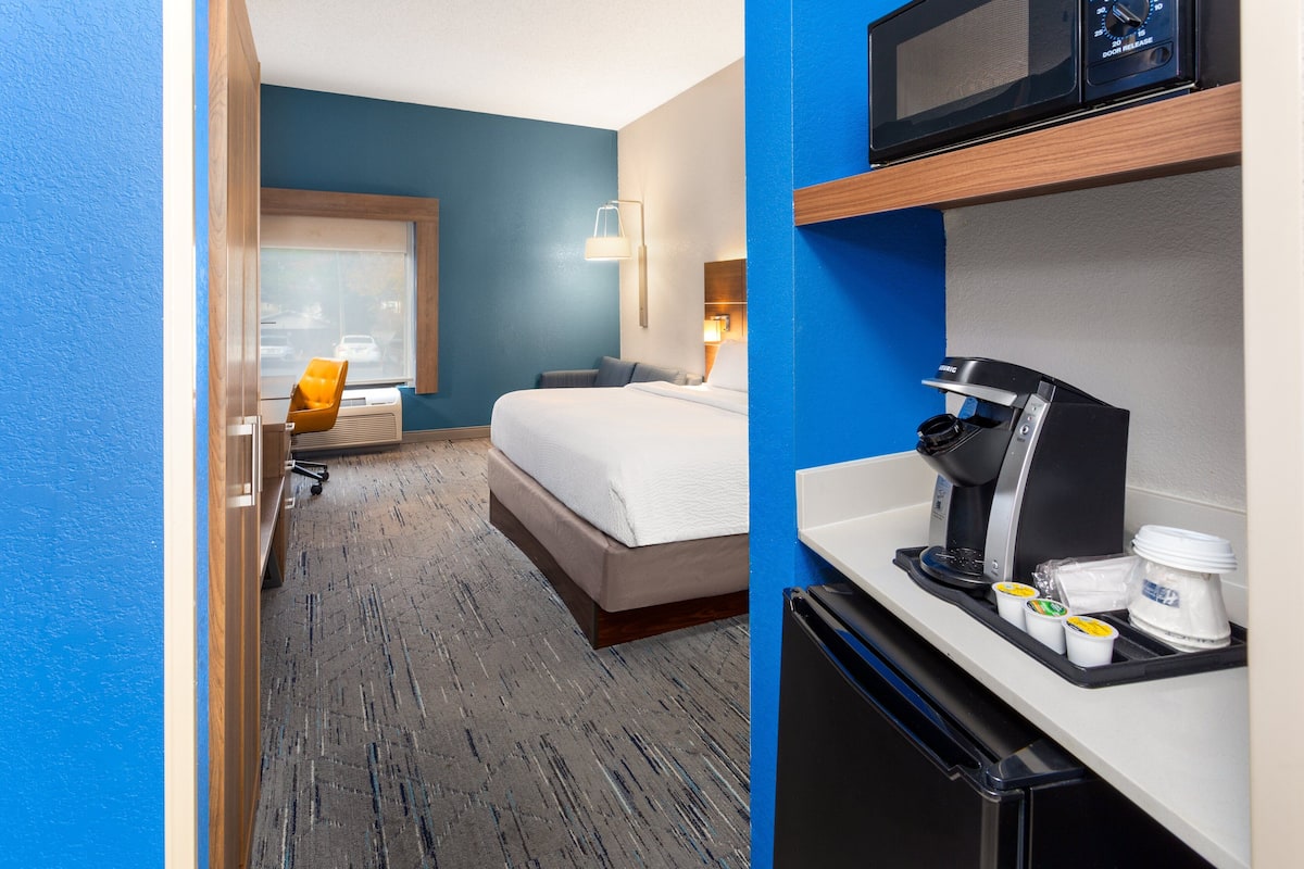 A hotel room with a bed, a desk with a coffee maker, a microwave, and a refrigerator.