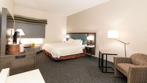 Ein Hotelzimmer mit einem großen Bett, Nachttischen mit Lampen, einem Sessel und einem Schreibtisch mit einer Lampe.
