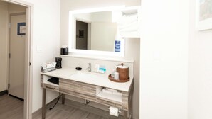Ein modernes Badezimmer mit Waschbecken, Spiegel und Handtuchhalter. Auf der Ablage steht eine Kaffeemaschine und ein Handtuchspender.