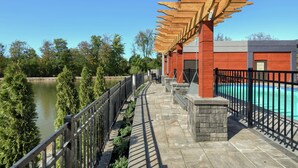 Un pont surmonté d’une pergola en bois, une piscine et une vue sur une rivière.